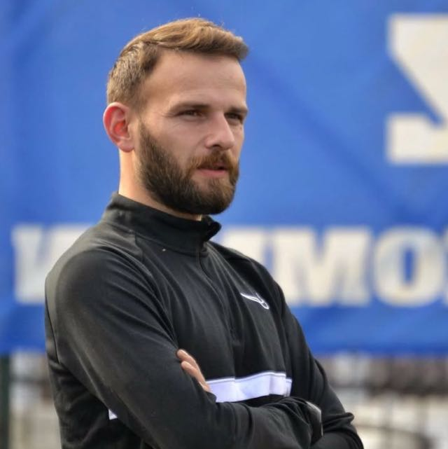 Close-up portrait of a young man with facial hair and a serious expression.